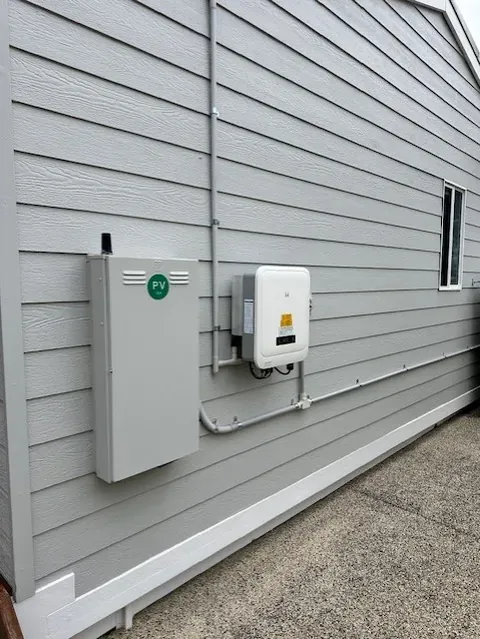 Solar inverter and DC isolators mounted on the side wall of a weatherboard house